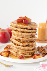 Stack of apple cinnamon pancakes with maple syrup on kitchen table with white background. Copy space. Close-up. Healthy homemade vegan breakfast food.