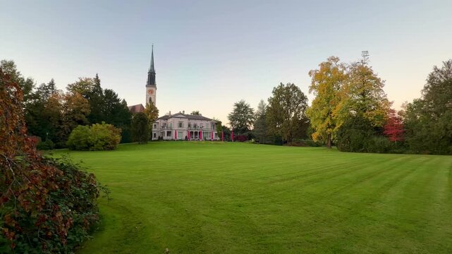 Villa Villette and church tower with large clock, photographed in Villette Park in Cham on Lake Zug in autumn, in the evening. The park is popular with nature lovers and families.