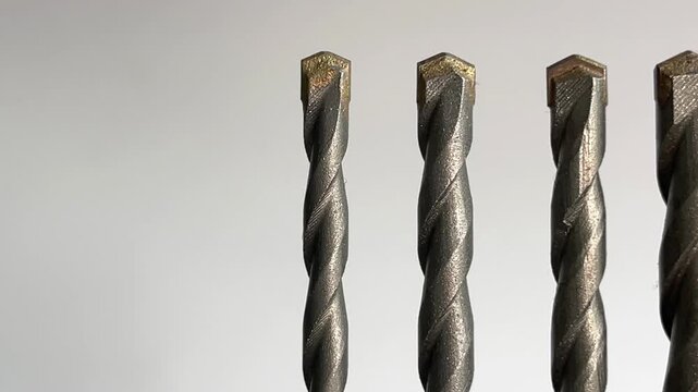 Metal drill bits arranged in a row on a light background, showing industrial tool texture and precision equipment for construction, repair, manufacturing, and hardware design projects
