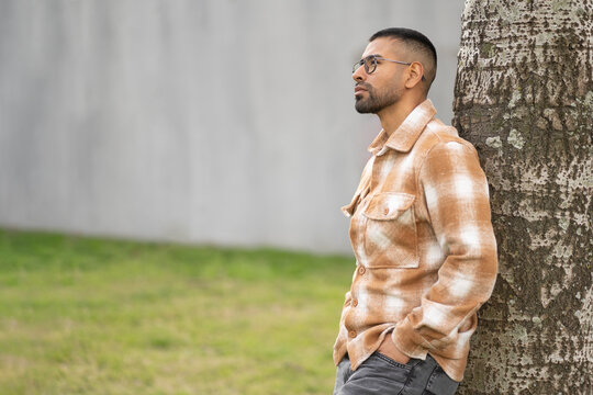 Thoughtful young latino man leaning against a tree in a quiet park