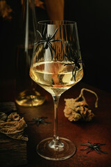 White wine in a clear glass with black spiders and dry leaves on rustic surface with dark background