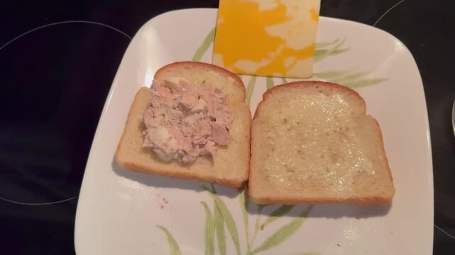 A young man is making a tuna and cheese sandwich for breakfast.