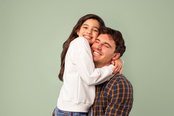 Love her most of all. Happy father with daughter embracing, hugging while posing over green background and smiling at camera