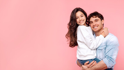 Fototapeta premium Happy father holding his preteen daughter, hugging and smiling at camera together, posing on coral background, panorama with free space
