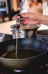 Woman hand holding digital thermometer measuring temperature of hot oil in frying pan in kitchen