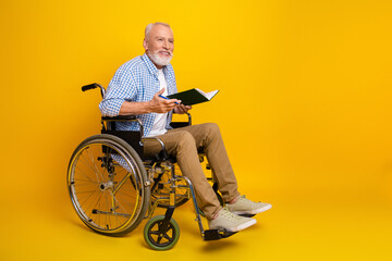 grandpa in wheelchair reads a book smiling against a bright yellow background in a warm rehab...