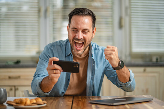 Happy man playing mobile game on smart phone at home