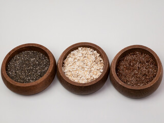 Chia, oat, and flax seeds in wooden bowls on a white background