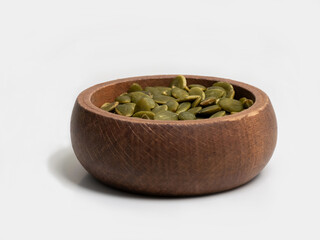Green pumpkin seeds in a rustic wooden bowl on a white background