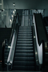 Modern escalator in a clean, minimalistic urban interior with cold lighting. The symmetrical lines and metallic textures create a futuristic and cinematic atmosphere. Ideal for use in architecture