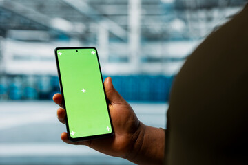 Close up of data center admin using green screen smartphone to monitor infrastructure network performance. Server room employee checks gear functionality using mockup mobile phone