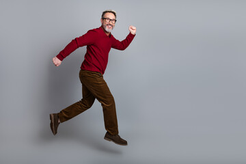Funny middle-aged businessman in stylish casual attire jumping against a gray background, showcasing active lifestyle
