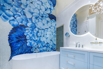 A stylish bathroom showcases a stunning blue floral mosaic wall, complemented by a sleek freestanding tub and contemporary sink. Soft lighting enhances the tranquil setting.