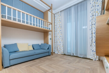 This bright and airy room features a comfortable blue sofa, a stylish bed, and large windows that let in natural light, creating a welcoming atmosphere.
