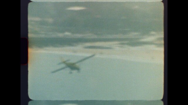 Retro biplane captured on 8mm film diving and banking above a calm ocean coastline with nostalgic film grain and soft focus
