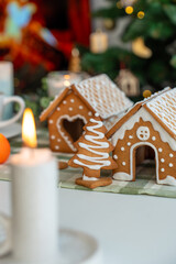 Handcrafted gingerbread village with decorated houses and Christmas tree cookie with white icing on festive table with bokeh lights. Holiday baking traditions, cozy celebration and sweet treats.