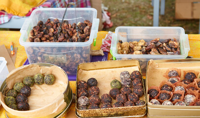 Assortment of handmade sweets, presented in variety of containers, includes round dried fruit candies with different textures and flavors, showcasing vibrant culinary experience at holiday market.