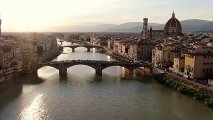 graceful drone video pans right over shimmering arno river, revealing florence's historic cityscape, duomo, giotto's bell tower at golden hour. majestic serenity