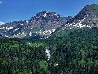 Mountain valley landscape featuring waterfall, forest, and snow