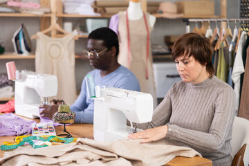 Working in sewing workshop - man and a woman working at sewing machines, creating new clothes