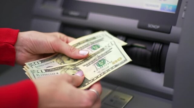 Extreme close-up video of a hand in a vibrant red long-sleeved shirt receiving crisp us twenty-dollar bills from a modern atm, blurred screen with bokeh. concept of financial transaction