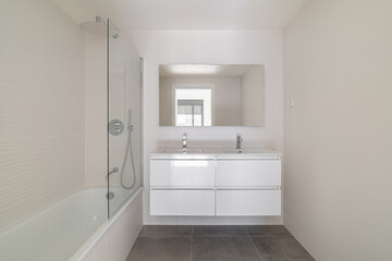 Modern bathroom with a white bathtub, sleek vanity, and large mirror. Neutral color scheme with natural light streaming in from a window.