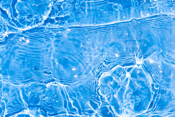 Blue water with ripples on the surface. Defocus blurred transparent blue colored clear calm water surface texture with splashes and bubbles. Water waves with shining pattern texture background.