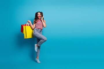 Excited young woman holding shopping bags in a fun and vibrant pose over a bright blue background...