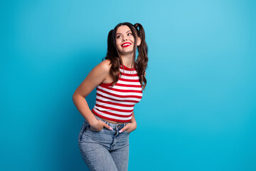 Stylish young woman with ponytails smiling happily in a striped top and jeans against a vibrant blue background