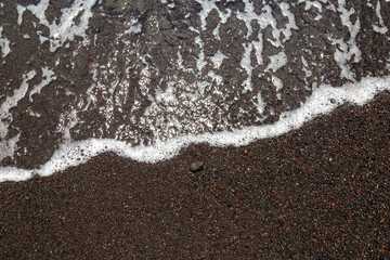 White sea foam lapping on the shore of a volcanic pebble beach, Tenerife, Spain,