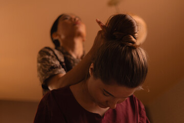 Asian female therapist giving thai massage to caucasian young woman in relaxing spa setting, warm tinting