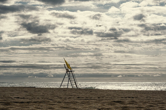 Lifeguard chair standing on deserted beach under stormy sky.