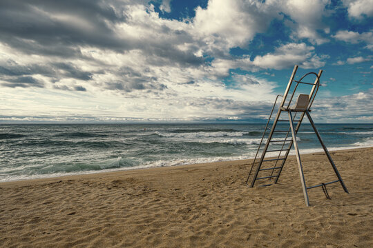 Lifeguard chair standing on empty beach under cloudy sky.