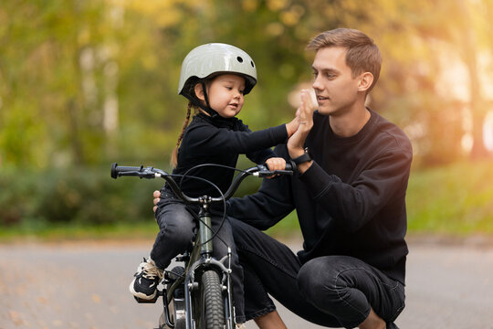 Father teaches daughter to ride bicycle in park, give each other high fives, support fatherhood concept