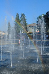 A child plays in a water fountain. Rainbows appear in the fountain sprays in the summer.
