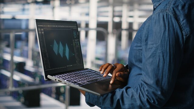 Close up of admin in data center using laptop to monitor neural network LLM visualization. Server hub IT expert overseeing rigs powering machine learning processes using notebook