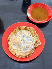 Roti Tampal - Roti Canai with Fried Egg and Curry Sauce on Red Plate