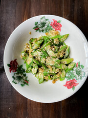 Home-cooked stir-fried okra with scrambled eggs served in a floral-rimmed white bowl on a dark wooden surface