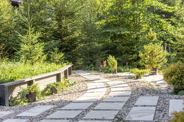 A serene garden path made of stone slabs winds through lush greenery. Small plants and trees line the pathway, creating a peaceful outdoor space.