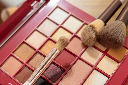 Makeup brushes resting on red palette filled with warm and nude tones. Elegant beauty composition showing professional cosmetic tools and textures for glamour, fashion, and skincare themes.