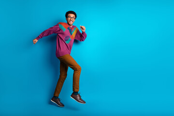 Young man in colorful sweater jumping joyfully against a vibrant solid blue background, expressing excitement and positivity