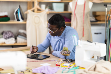 African American man tailor creates sketch of dress on tablet, draws and visualizes model of clothing using computer technology. Software for drawing and visualization.