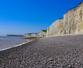 Seven Sisters chalk cliffs towering over the pebble beach and sea, iconic coastal landscape in East Sussex, England. East Sussex, England