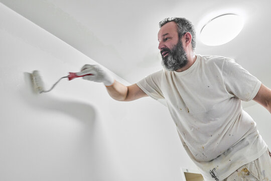 Close up of painter rolling fresh white paint on wall - Powered by Adobe