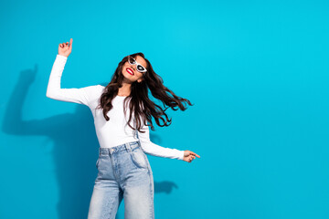 Happy young woman with flowing brunette hair enjoying dancing with stylish look on a vibrant blue...