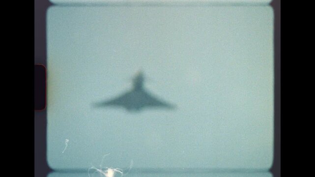 Authentic old film capturing the silhouette of a military fighter jet approaching through a hazy sky, featuring genuine super 8mm grain, scratches, and light leaks for a retro, historical feel