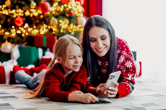 Happy mother and daughter bonding during Christmas holiday with phone, amid festive decorations and gifts at home - Powered by Adobe