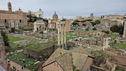 Obraz premium Rome, Italy - 13 January 2025. The Temple of Castor and Pollux rises at the Forum amid ruins, visitors, and the Curia Julia, with the Altar of the Fatherland and Capitoline Hill in the distance.