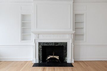 A fireplace with a pattern marble surround, black brick hearth,  with a wainscoting wall, and a white decorative mantel surrounded by shelving.