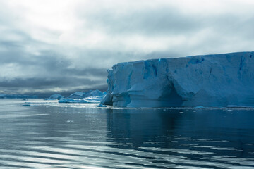 Towering melting iceberg in Arctic icy ocean. Snow covered glacier drift under blue sunny sky. Pure ice floats in turquoise water. Ecology, melting ice, climate change global warming. Aerial view